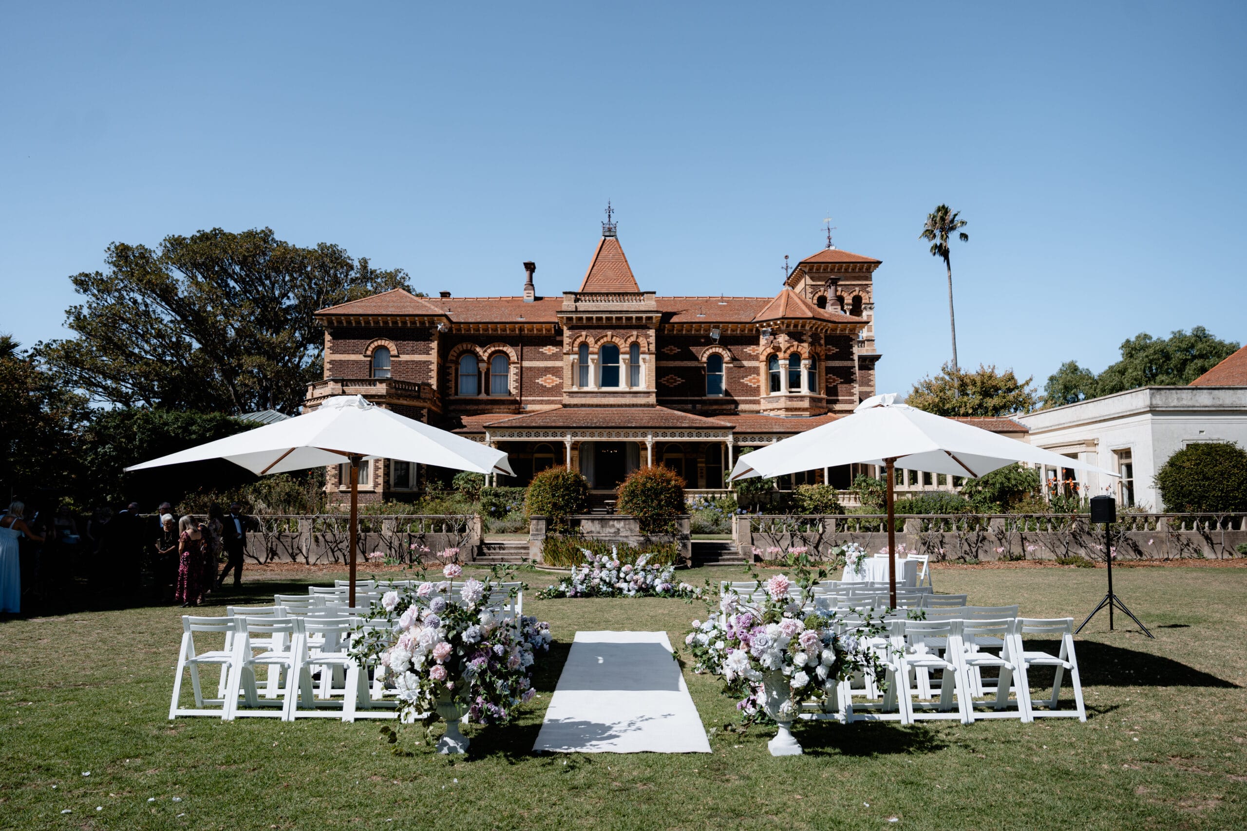 Rippon Lea Estate, Central Lawn - Ceremony set-up with white wooden chairs, large white garden umbrellas, and signing table with cloth 
